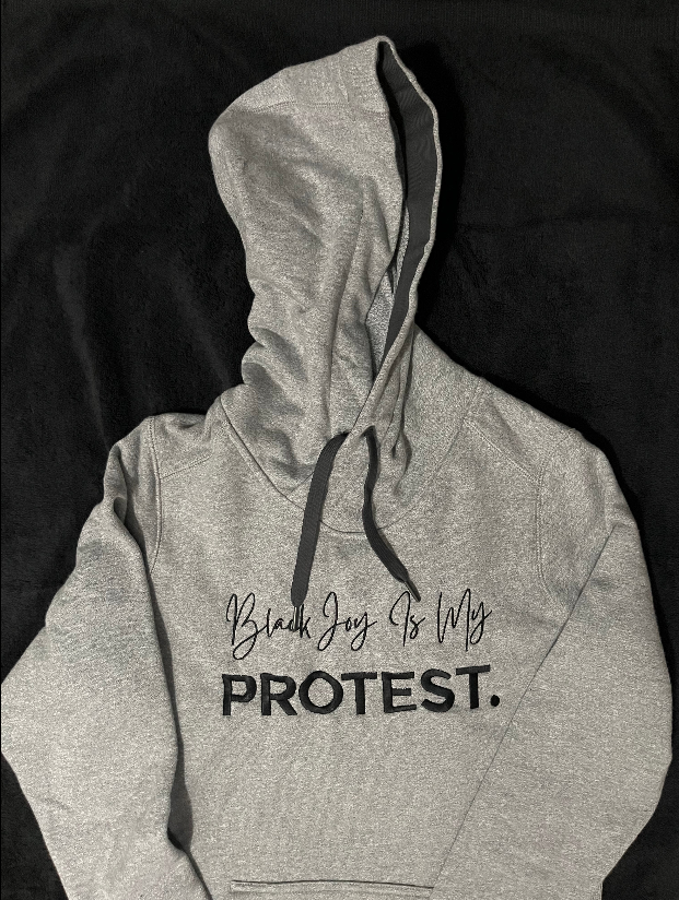 Gray hoodie with 'Black Joy Is My Protest' text on a black background