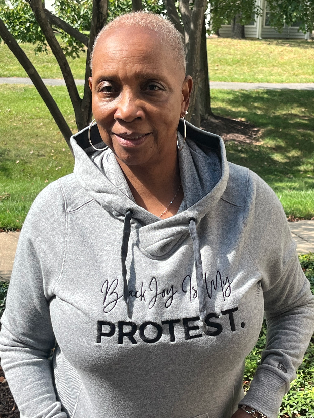 Woman wearing a gray hoodie with 'Black Joy Is My Protest' text outdoors.