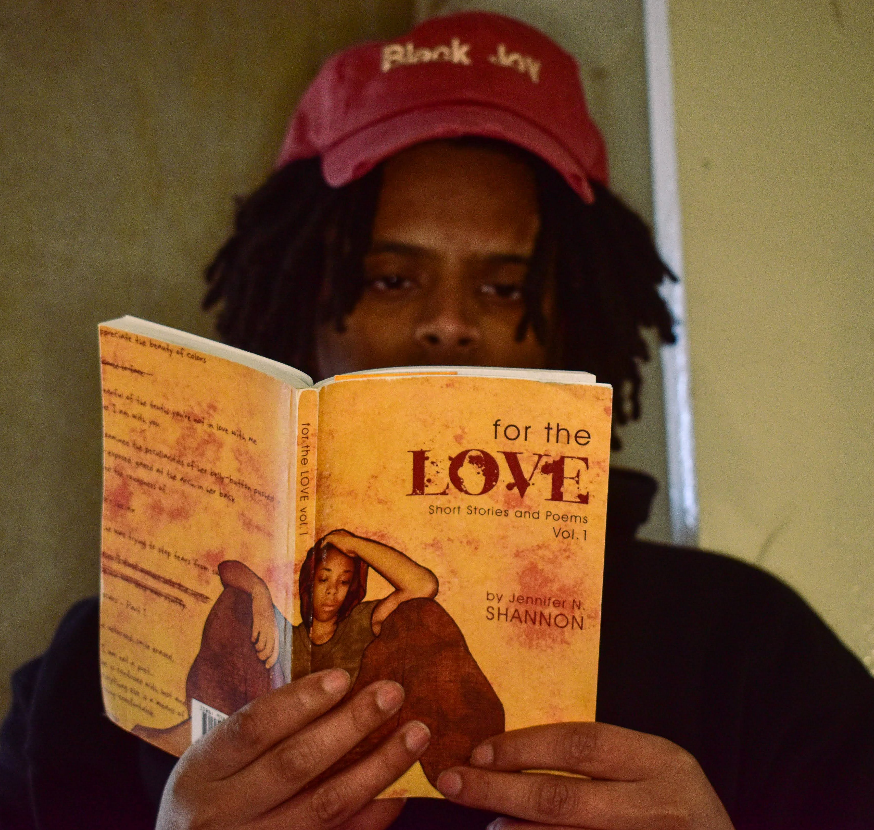 Person holding a book titled 'For the Love' by Jennifer Shannon, wearing a red cap with 'Black Joy' text.
